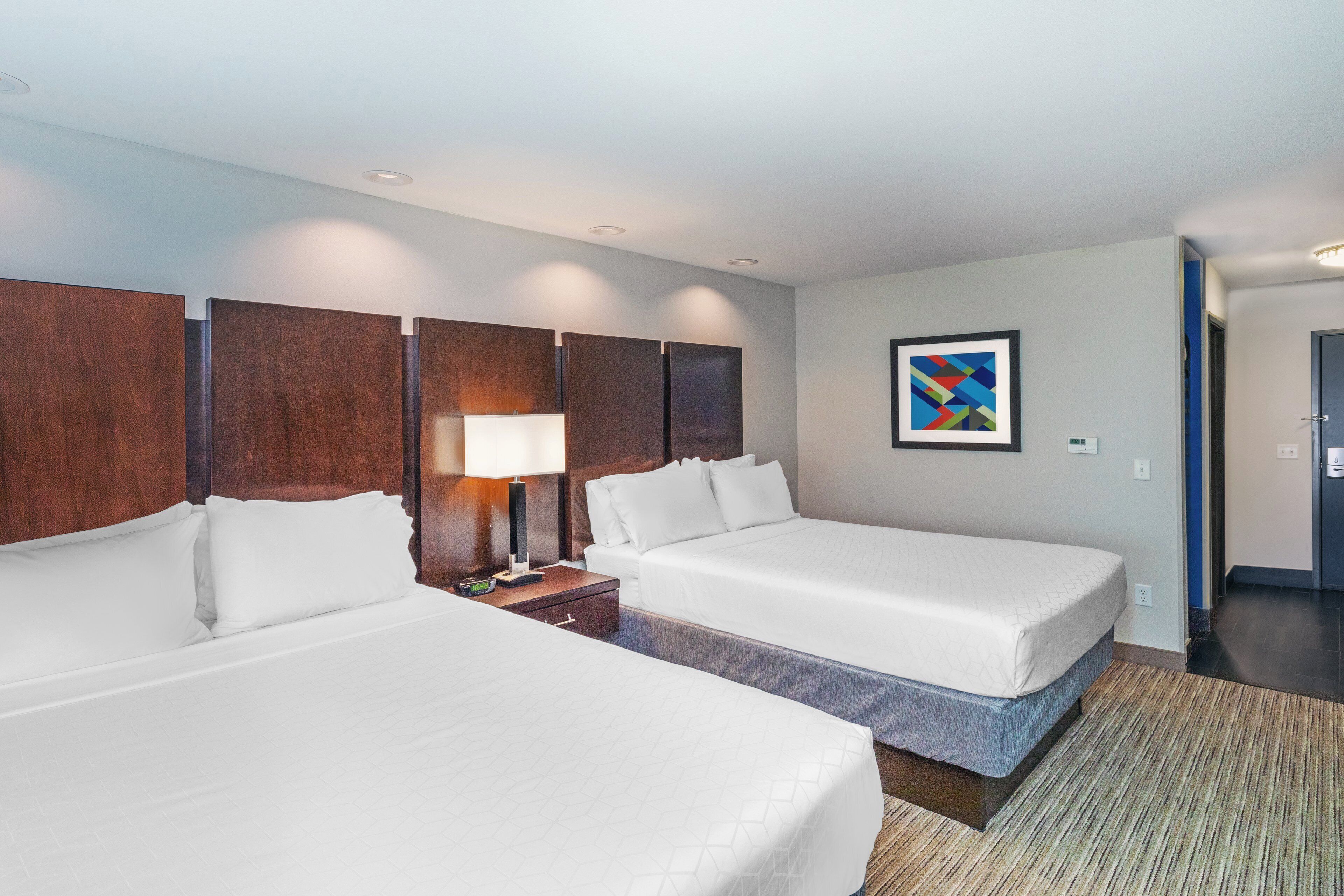 A hotel room with two beds, a nightstand, a lamp, and a painting on the wall.