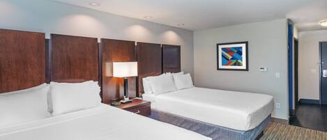 A hotel room with two beds, a nightstand, a lamp, and a painting on the wall.