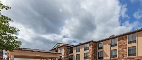 Un hotel con fachada de ladrillo, varios balcones y una zona de estacionamiento cubierta.