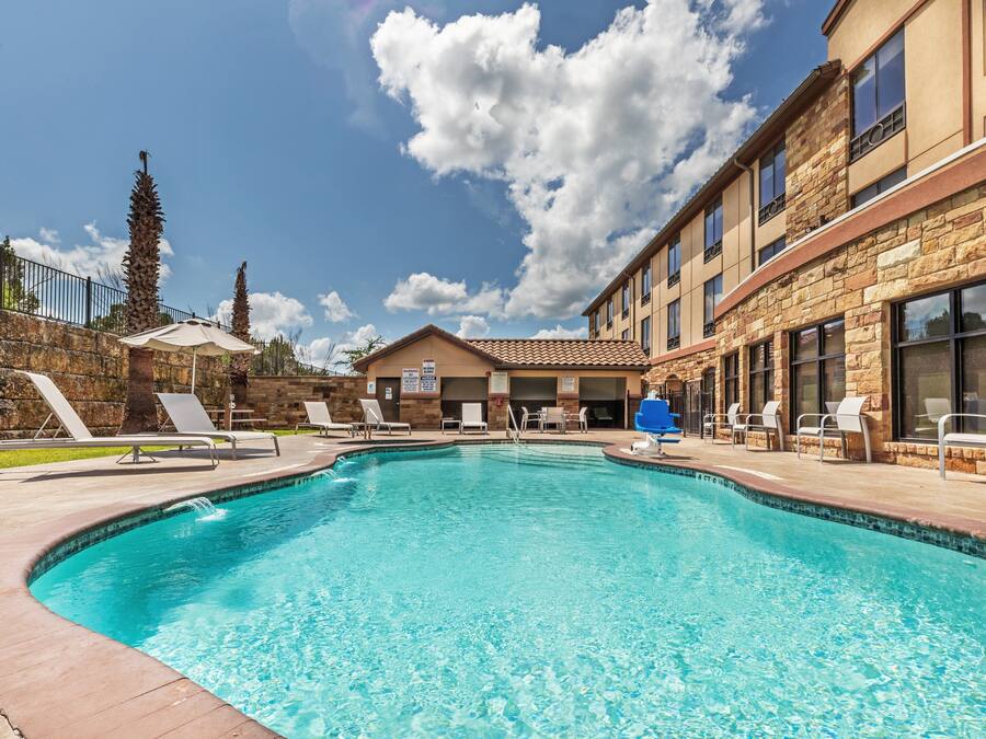 Una piscina con sillones de descanso y un edificio de fachada de piedra.