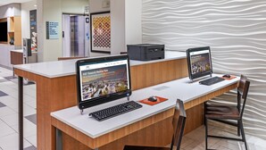 A reception desk with two laptops, a printer, and a computer monitor. There is a sign indicating the business center and a wall with a wavy pattern.