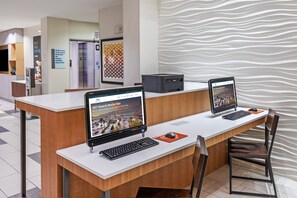 A reception desk with two laptops, a printer, and a computer monitor. There is a sign indicating the business center and a wall with a wavy pattern.