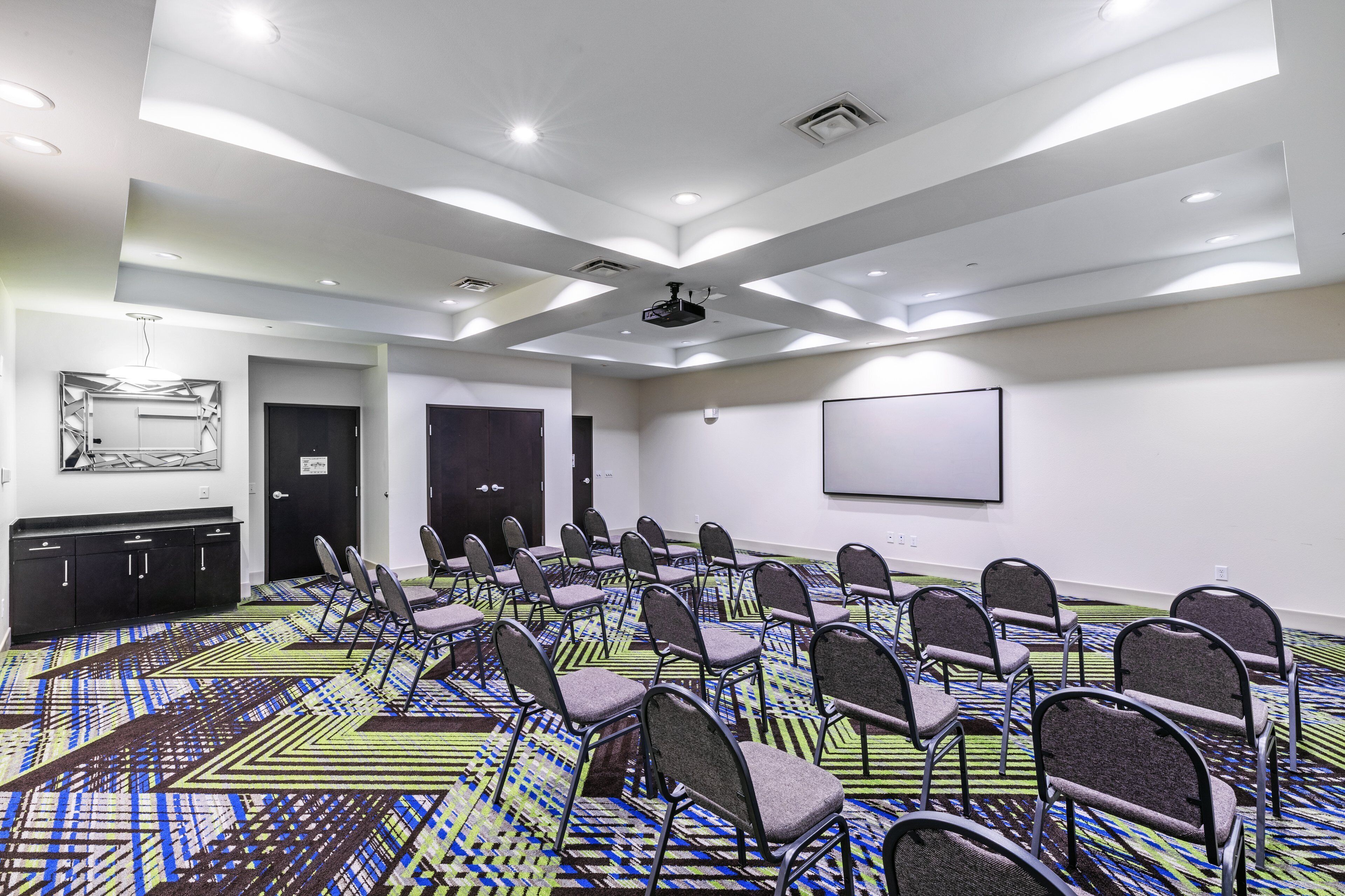 A conference room with rows of chairs, a projector screen, and a patterned carpet.