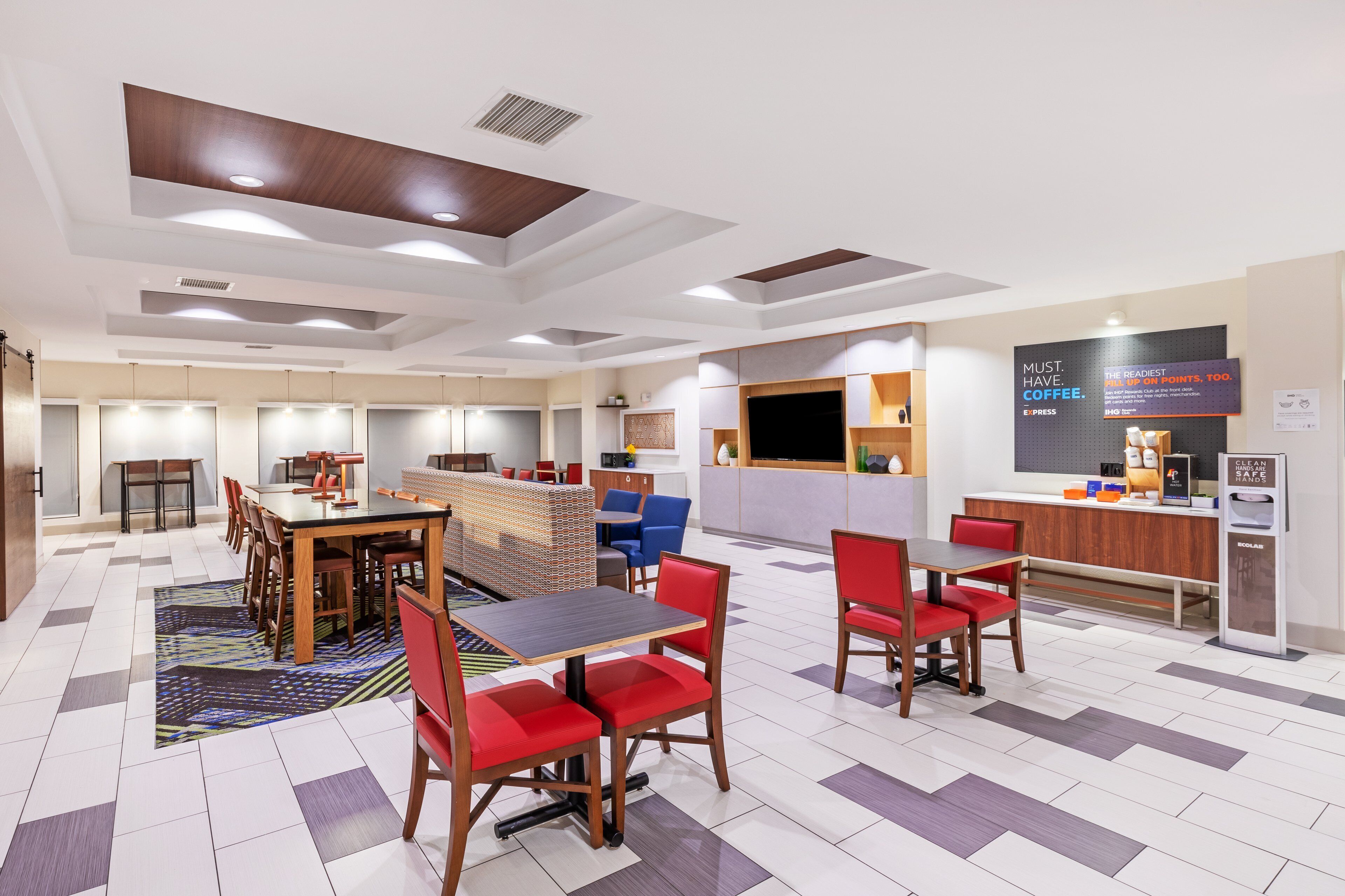 A modern hotel lobby with a central seating area, a coffee station, and a reception desk.