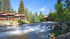 A cabin-style hotel with a river in front, surrounded by trees and mountains. - Boulder Brook on Fall River (Estes Park)