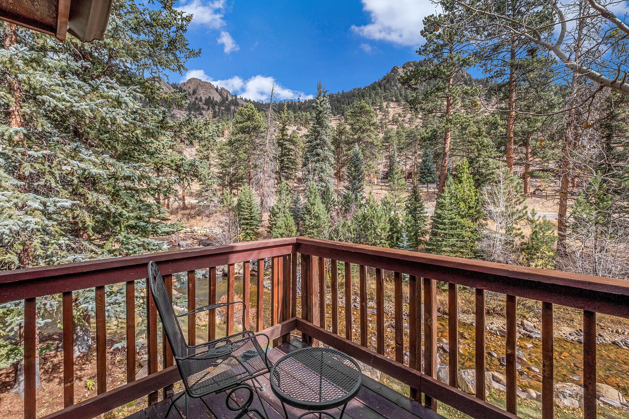 A wooden deck with a metal table and chairs overlooking a forested mountain area.