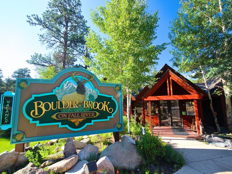 A sign for Boulder Brook on Fall River with a wooden cabin in the background.