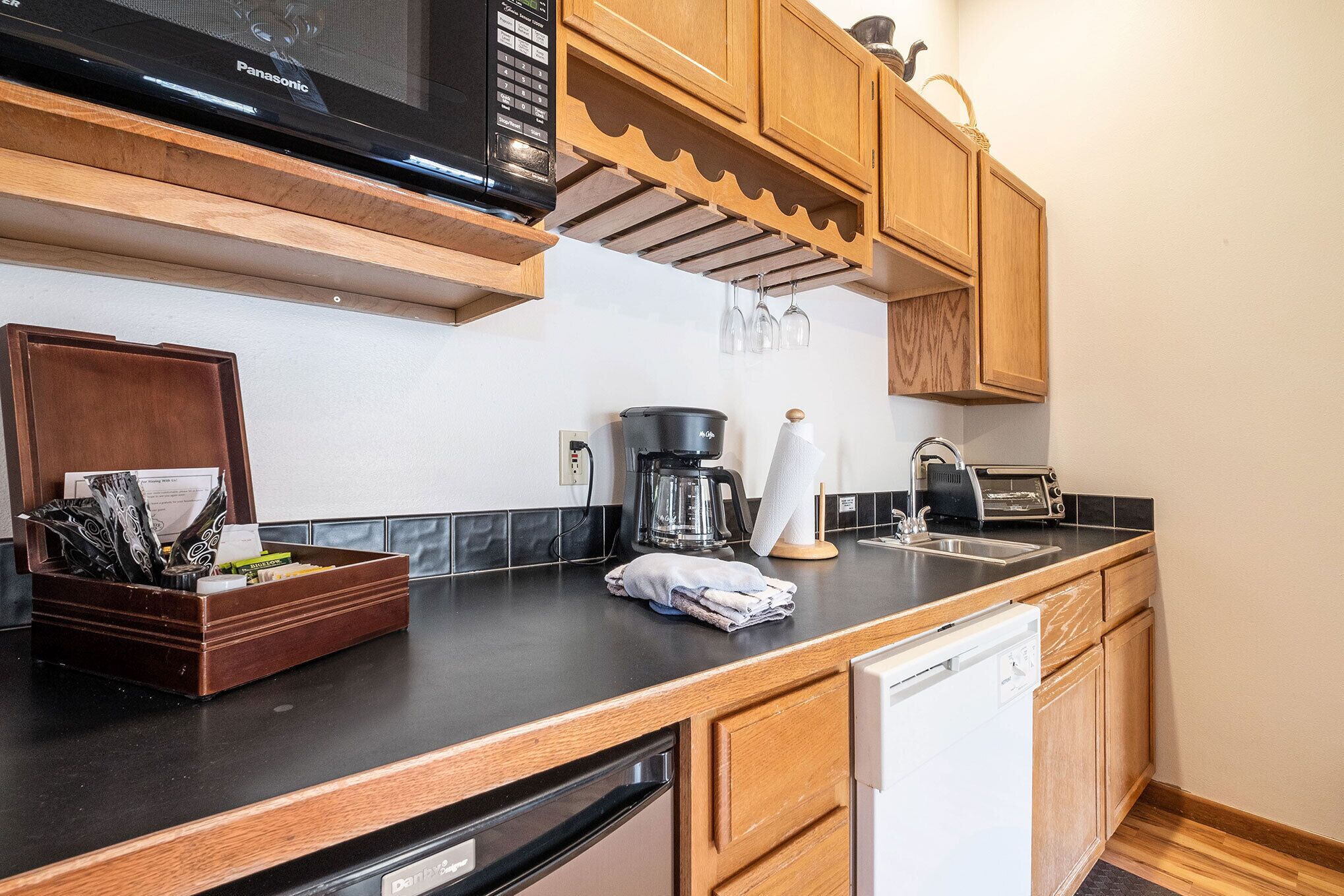 A compact kitchen with wooden cabinets, a microwave, a coffee maker, and a dishwasher.