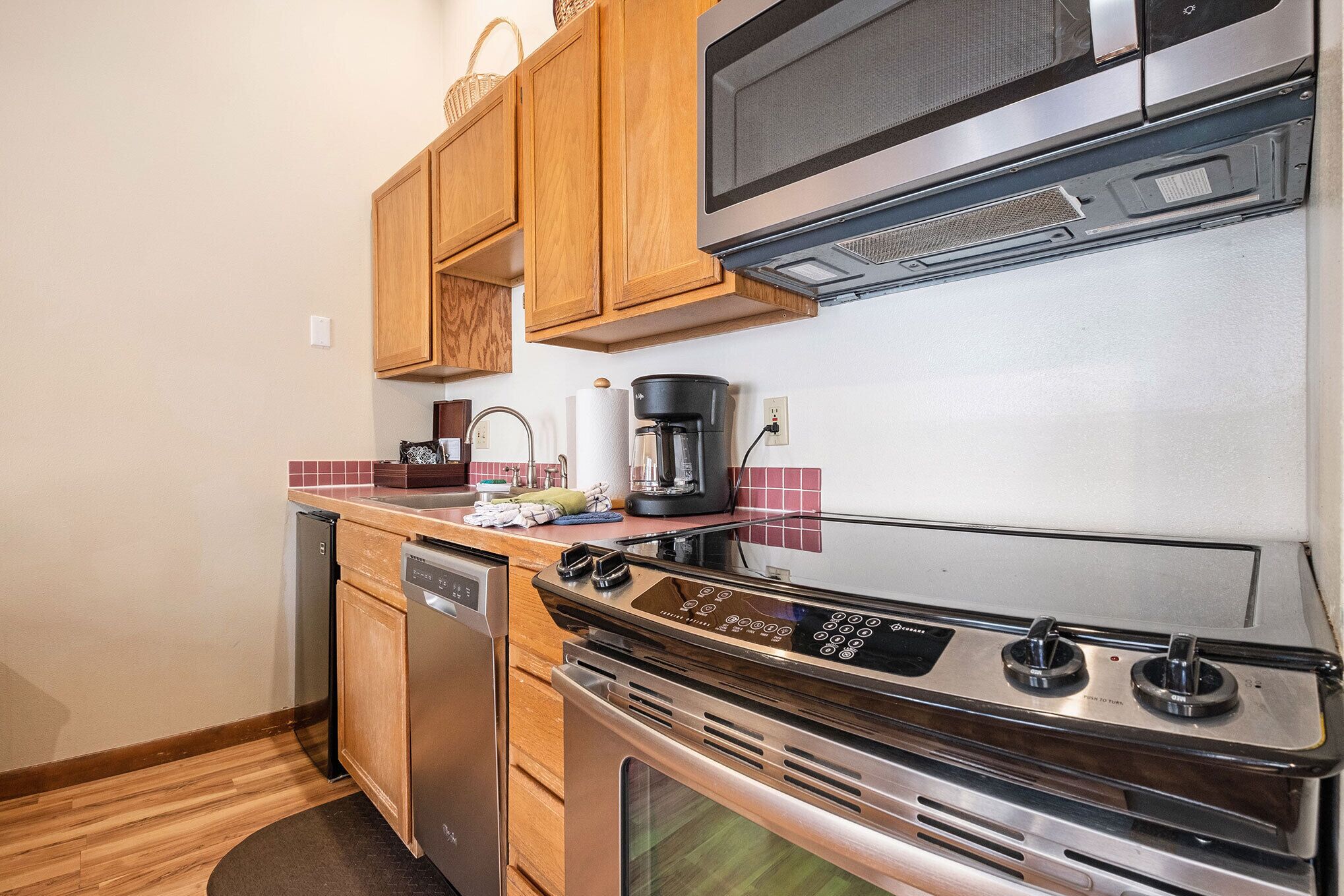 A compact kitchen with wooden cabinets, a stainless steel stove, a dishwasher, and a microwave.
