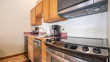 A compact kitchen with wooden cabinets, a stainless steel stove, a dishwasher, and a microwave.