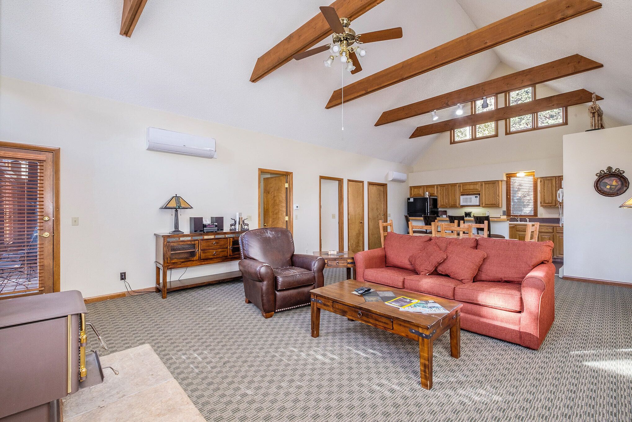 Ein geräumiges Wohnzimmer mit hohen Decken, Holzbalken, einem roten Sofa, einem Ledersessel und einem Couchtisch aus Holz.