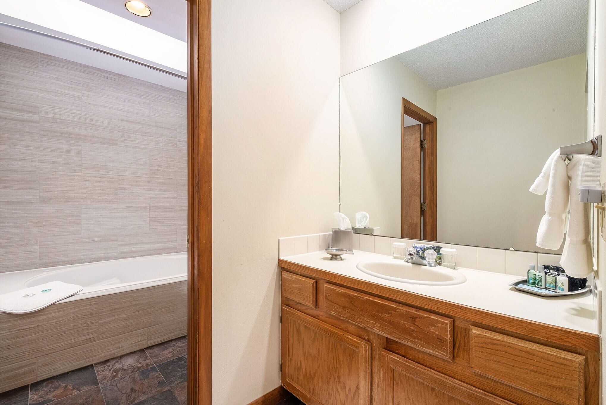 A modern bathroom with a wooden vanity, a large mirror, and a bathtub.