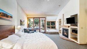 A bedroom with a large bed, a TV, a fireplace, and a view of the outdoors. - Boulder Brook on Fall River (Estes Park)