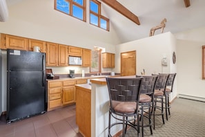 A kitchen with wooden cabinets, a black refrigerator, a microwave, and a coffee maker. There are four bar stools with cushioned seats.