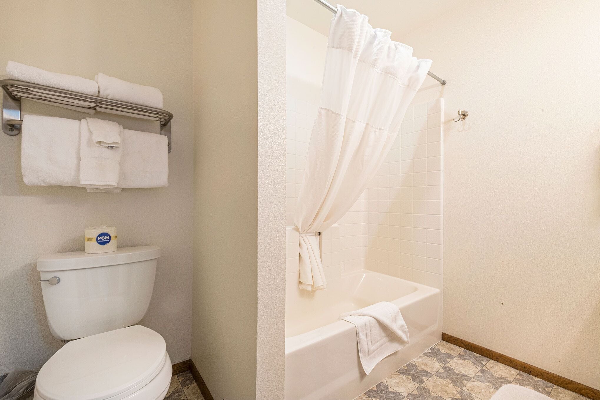 Un baño con inodoro, bañera con cortina de ducha y toallero con toallas dobladas.