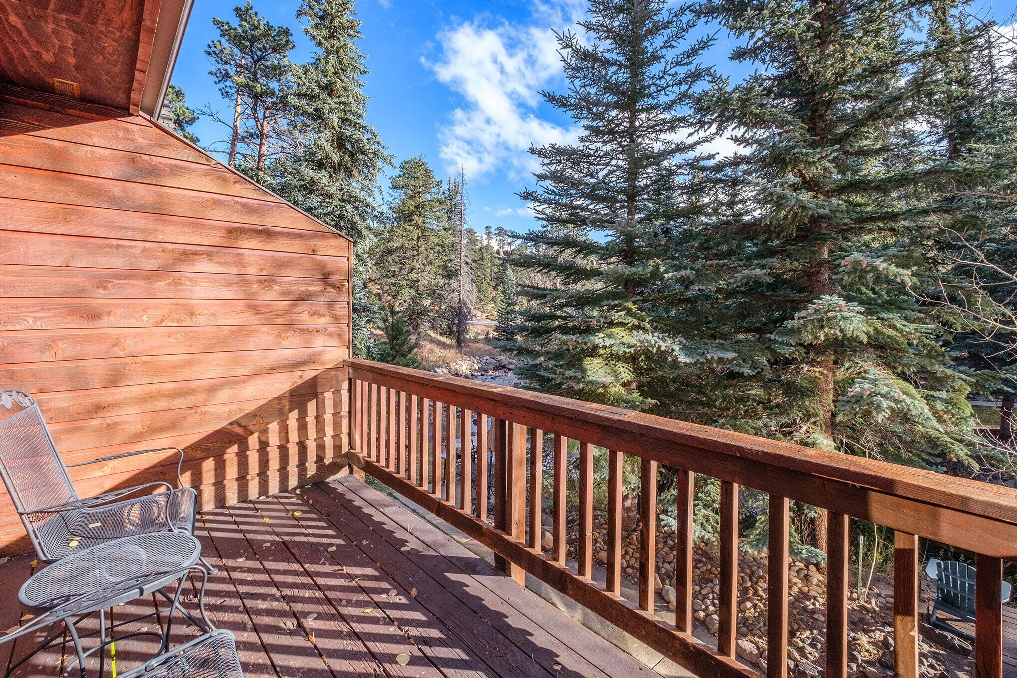 A wooden deck with a metal chair, surrounded by a wooden railing, overlooking a forested area.
