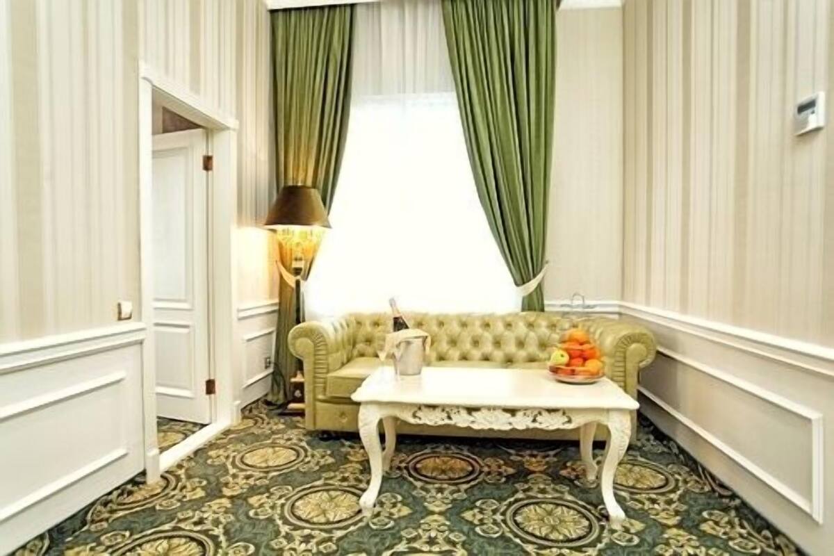 A room with a sofa, a table with a bowl of fruit, a lamp, and a window with green curtains.