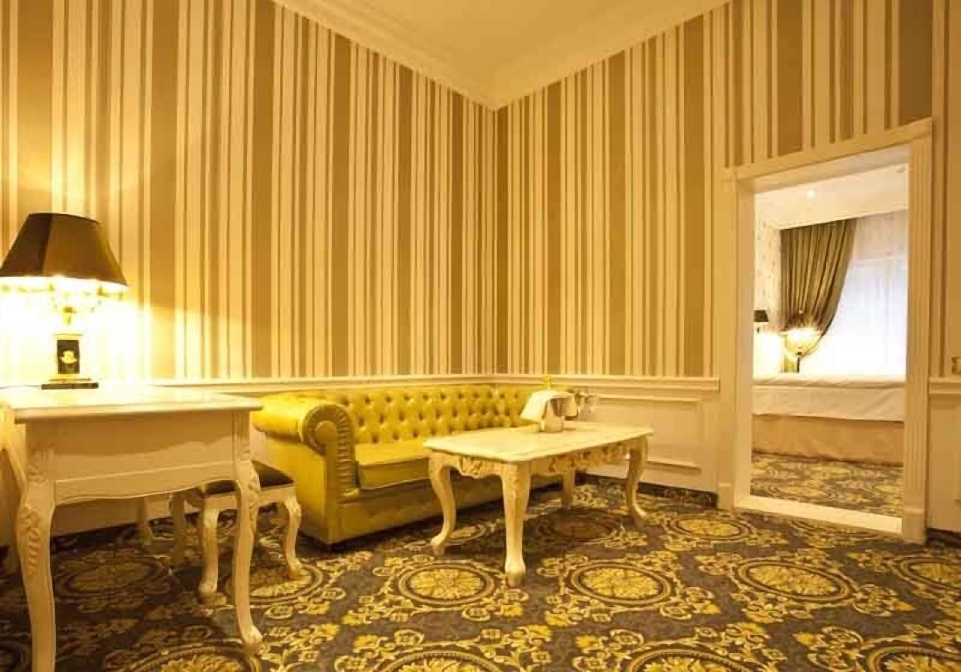 Een kamer met gestreepte behang, een gele bank, een witte tafel en een kamerbreed tapijt met dessin.