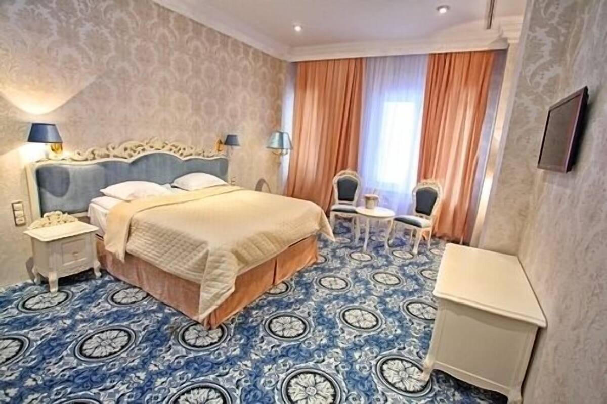 A hotel room with a large bed, two bedside tables, a small table with chairs, and a large window with curtains.