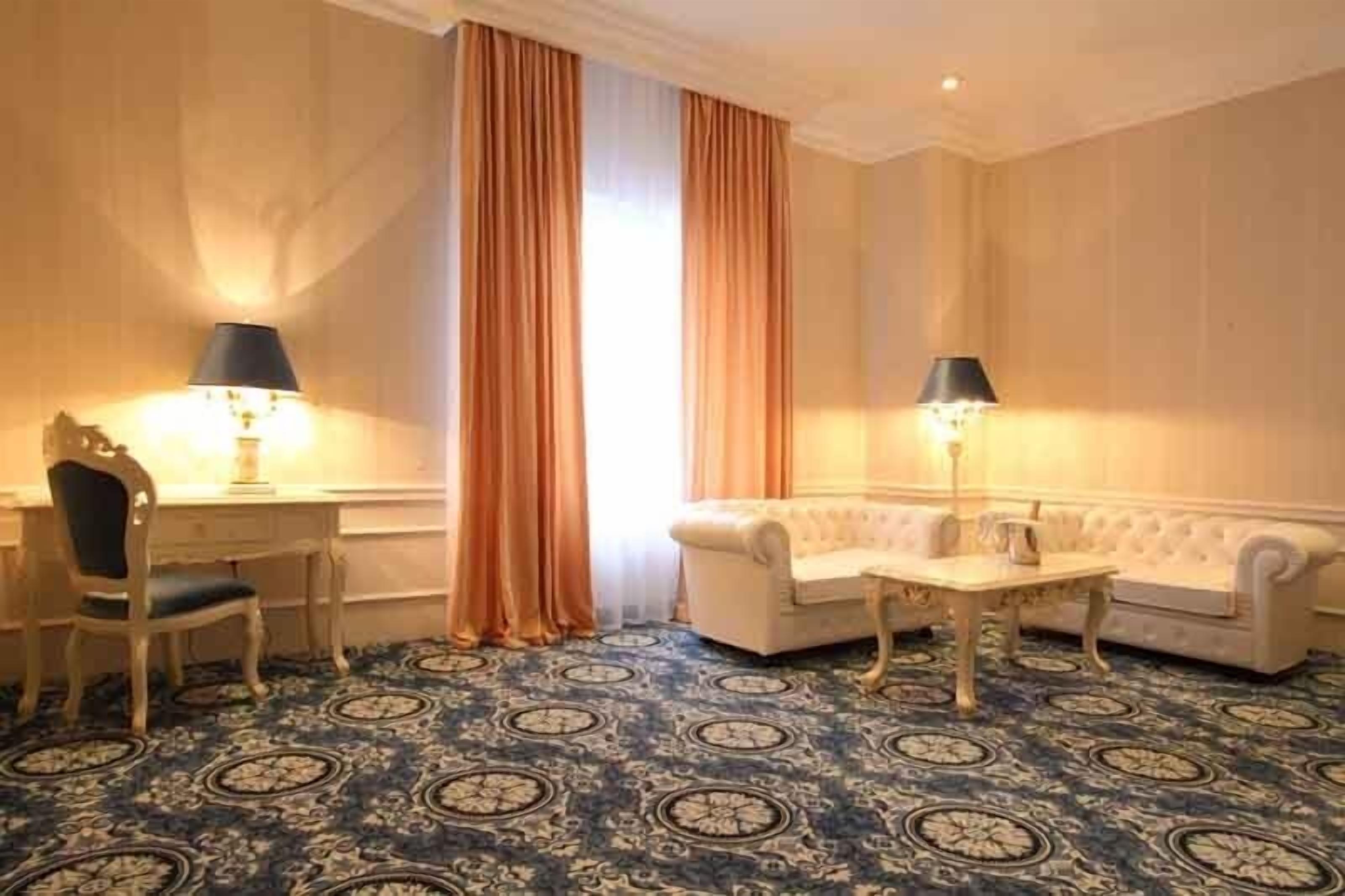 A room with a patterned carpet, a sofa, a chair, and two lamps.