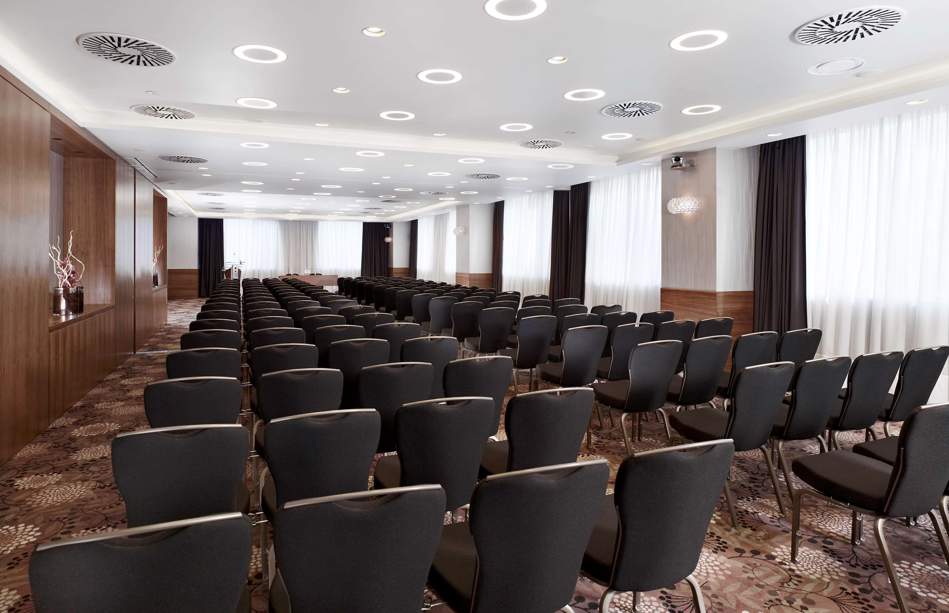Ein Konferenzraum mit Reihen von Stühlen, einem gemusterten Teppich und einer Decke mit runden Leuchten.