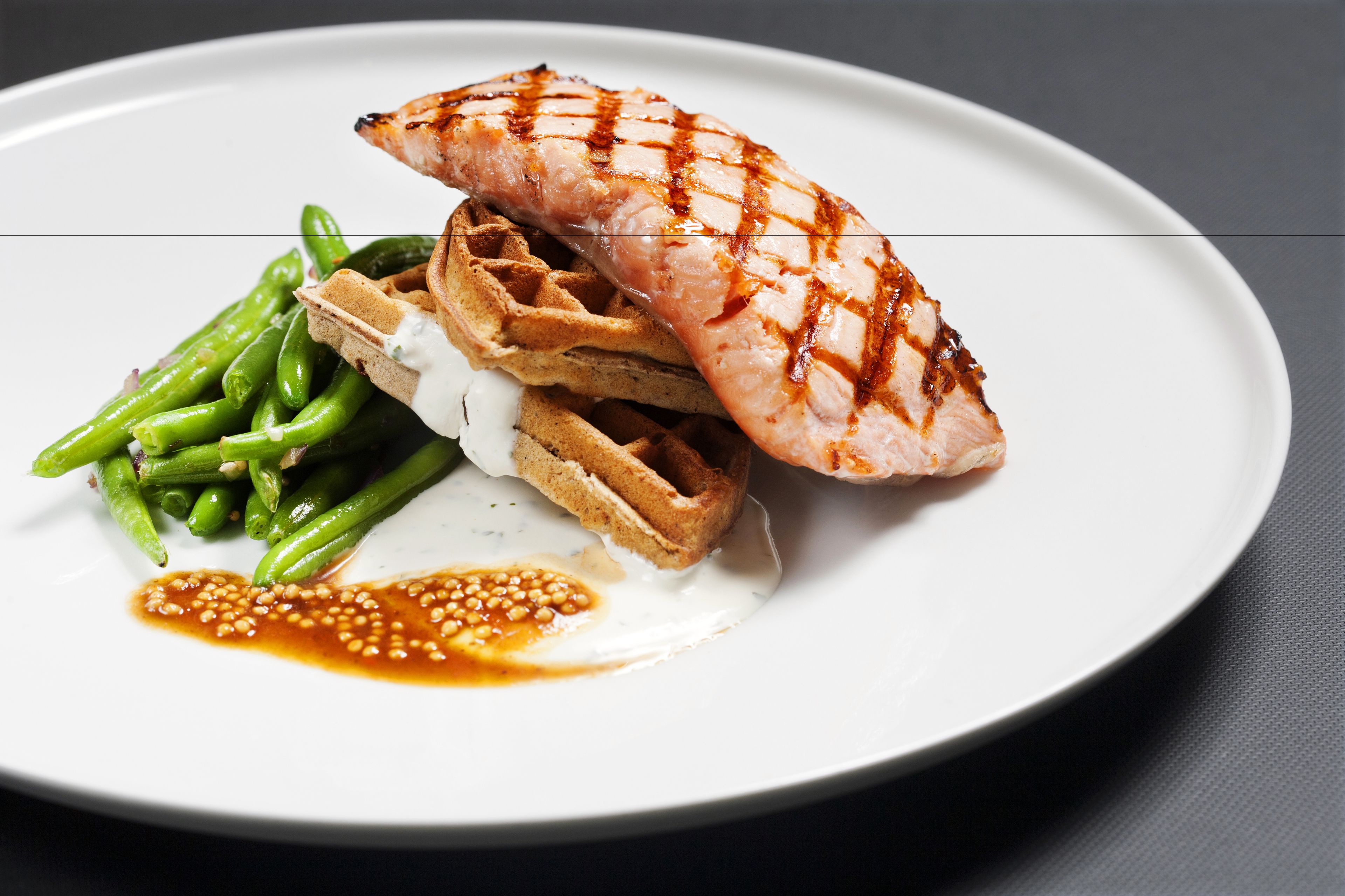 A plate with grilled fish, green beans, waffles, and a sauce.