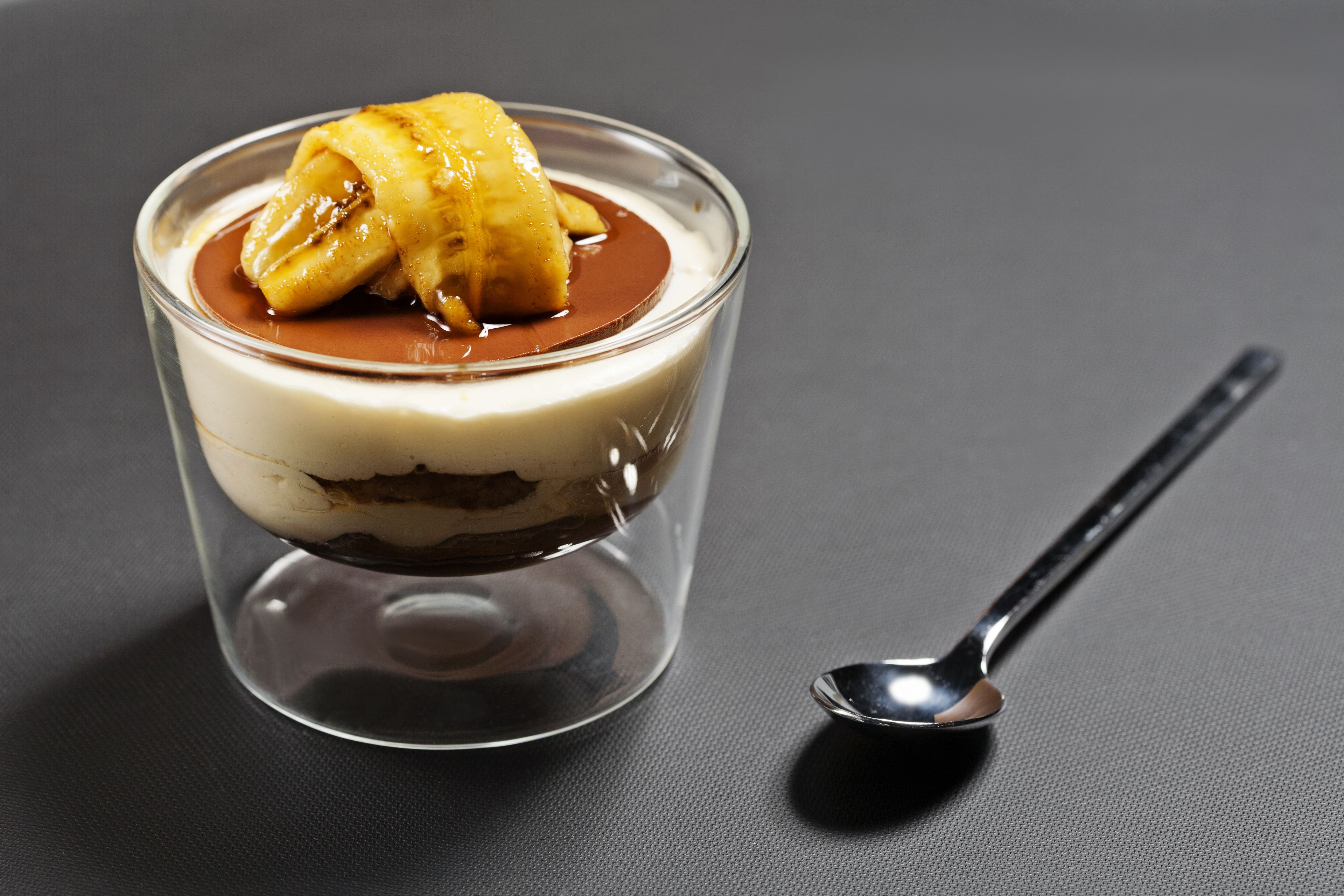 Un postre en un vaso transparente, con una cuchara al lado.