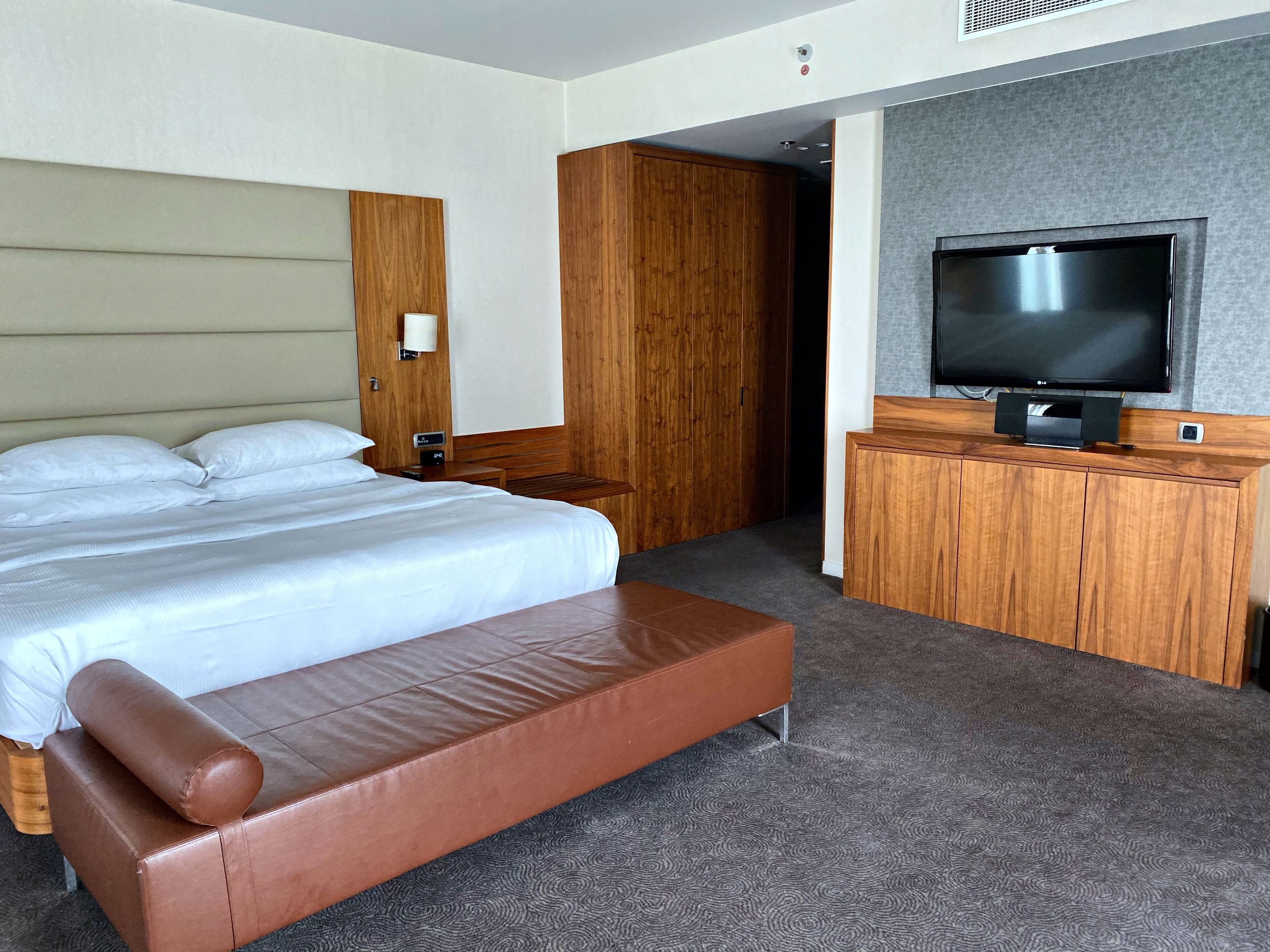 A hotel room with a bed, a wooden wardrobe, a television, and a bench.