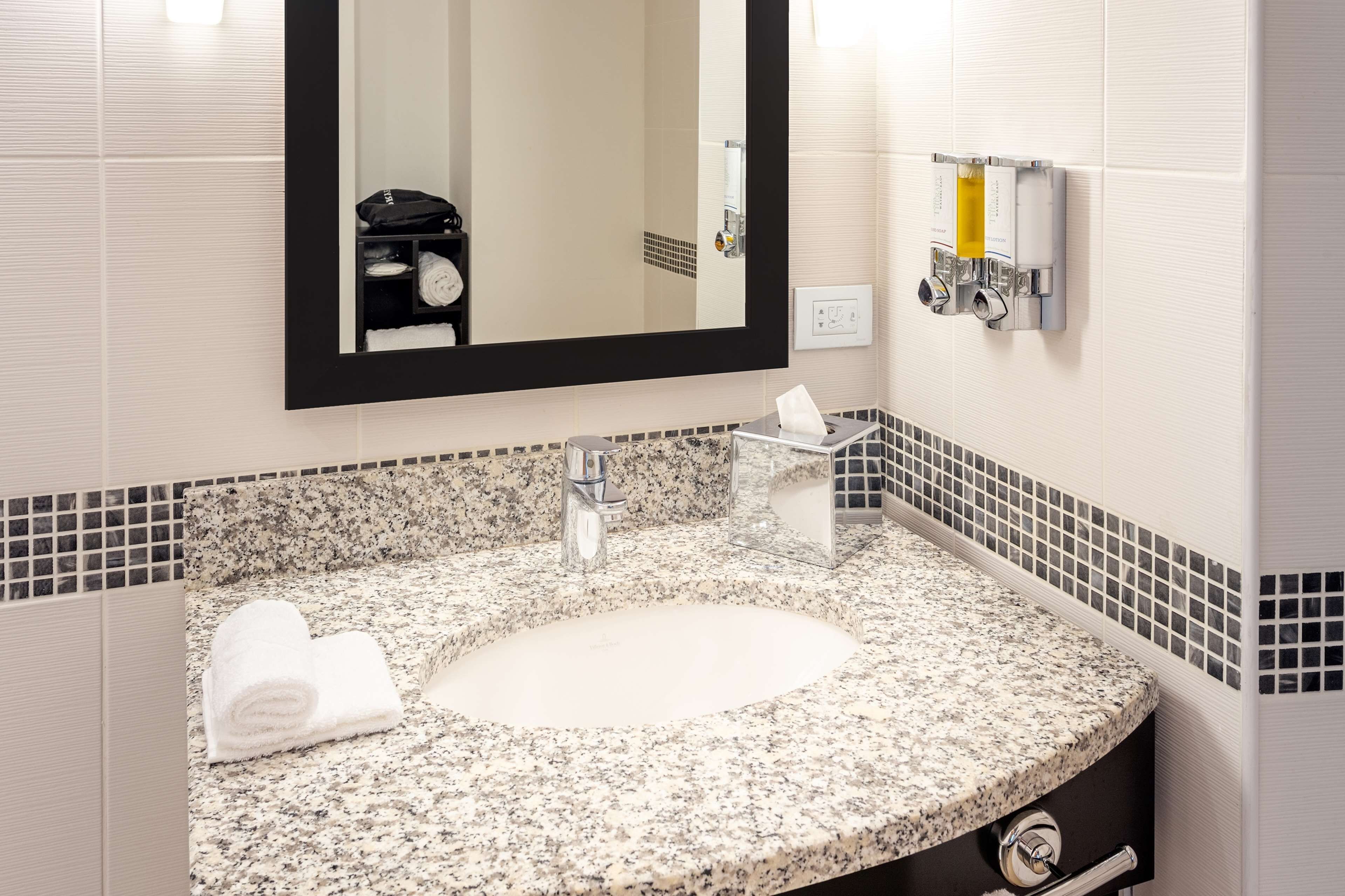 Un baño con lavamanos de encimera de granito, un espejo grande y un perchero para toallas.