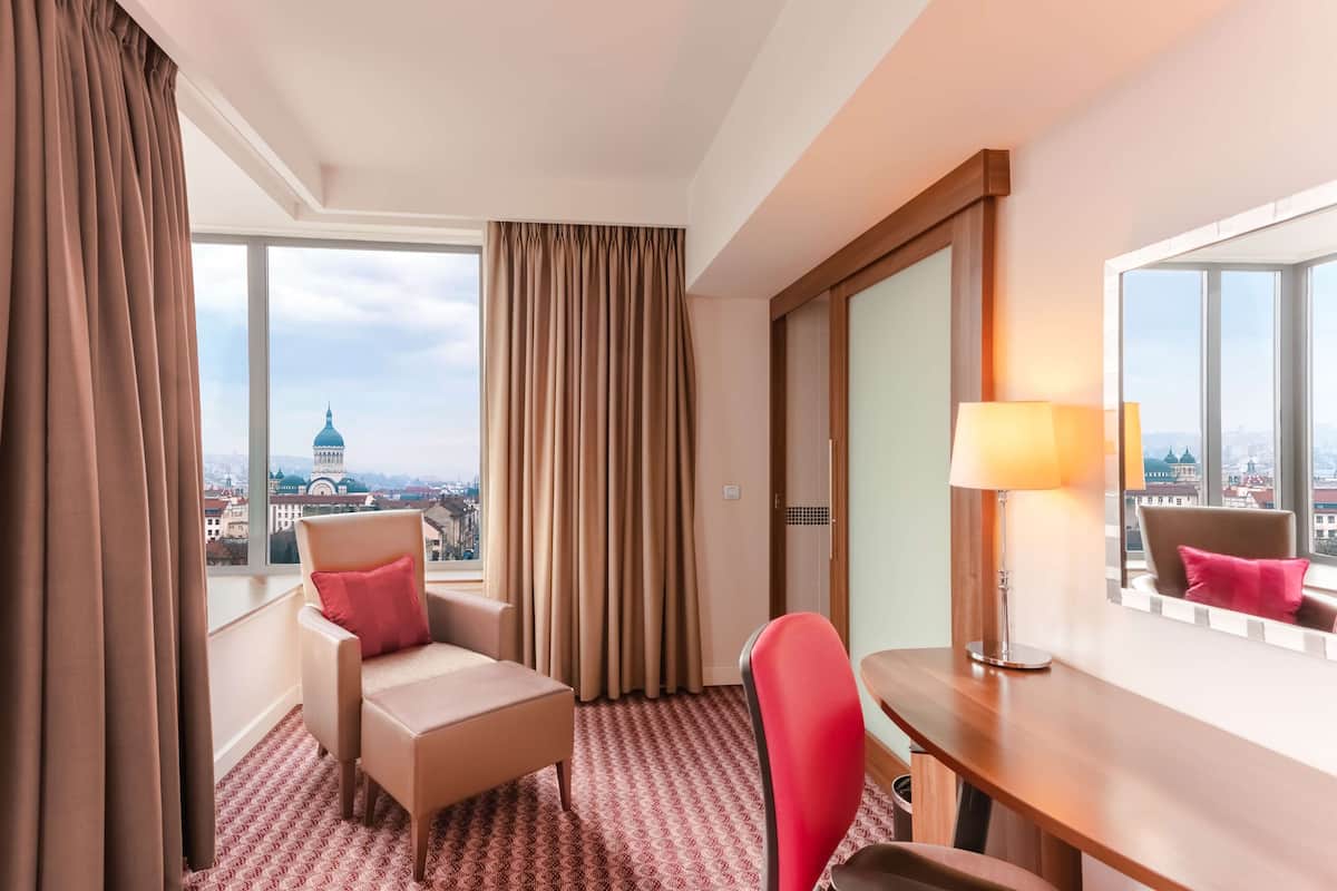 Une chambre d’hôtel avec une grande fenêtre, un bureau, une chaise et un lit.