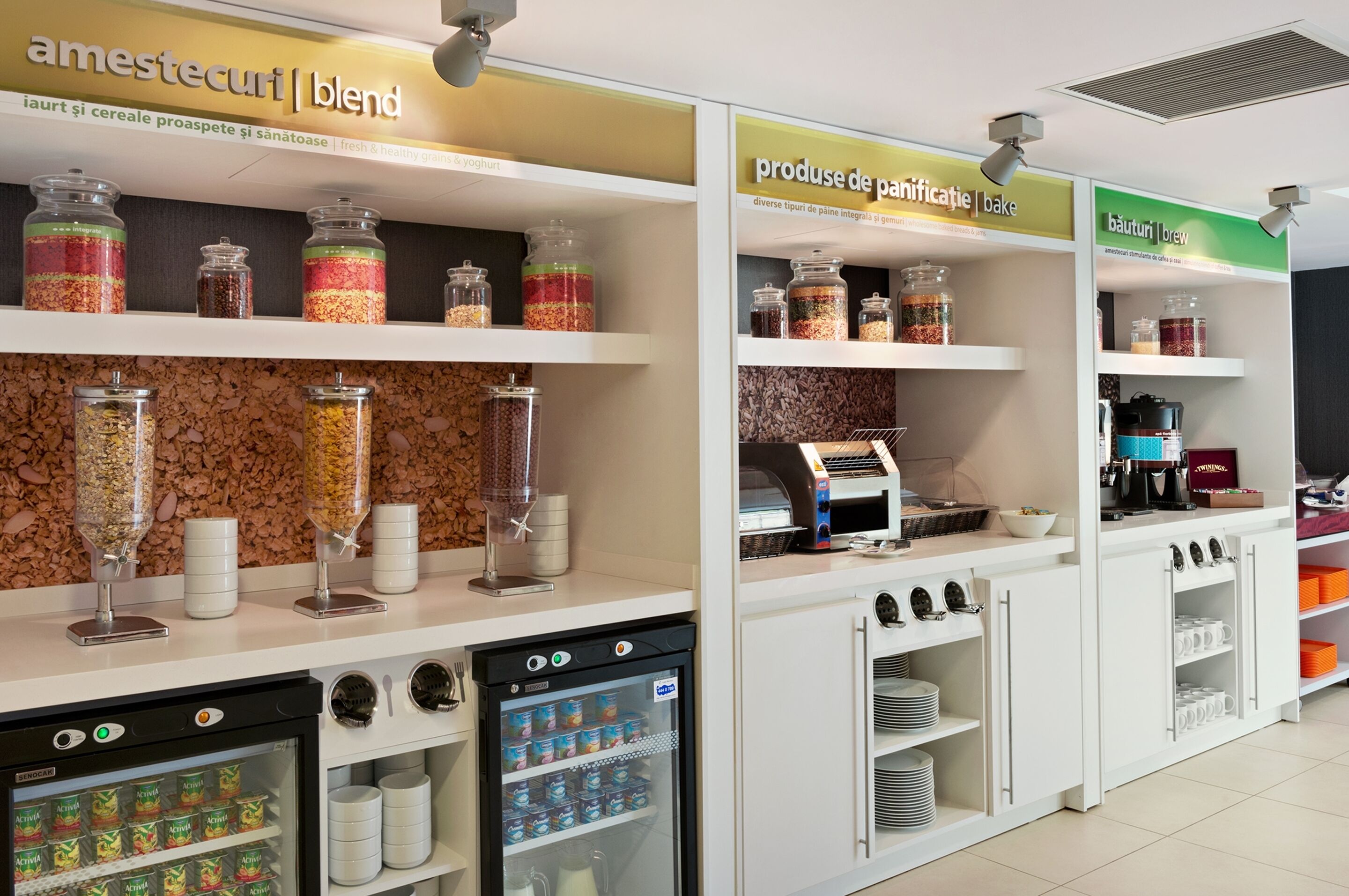 A breakfast bar with jars of granola, cereal, and yogurt, a coffee machine, and a refrigerated display of yogurt cups.