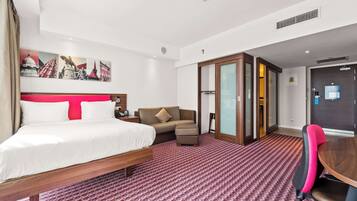 A hotel room with a bed, a sofa, a dining table, and a chair.