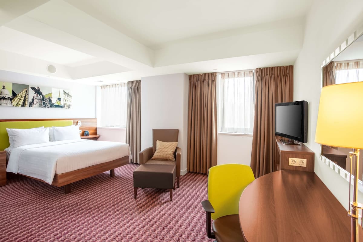 Une chambre d’hôtel avec un lit, une chaise, une table, un téléviseur et une lampe.