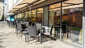 An outdoor cafe with tables and chairs, large windows, and a covered patio area. - Hampton by Hilton Cluj-Napoca (Cluj-Napoca)