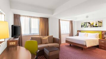 A hotel room with a bed, a sofa, a TV, a desk, and a chair.