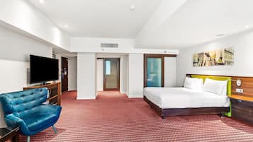 A hotel room with a bed, a television, a blue armchair, and a red patterned carpet.