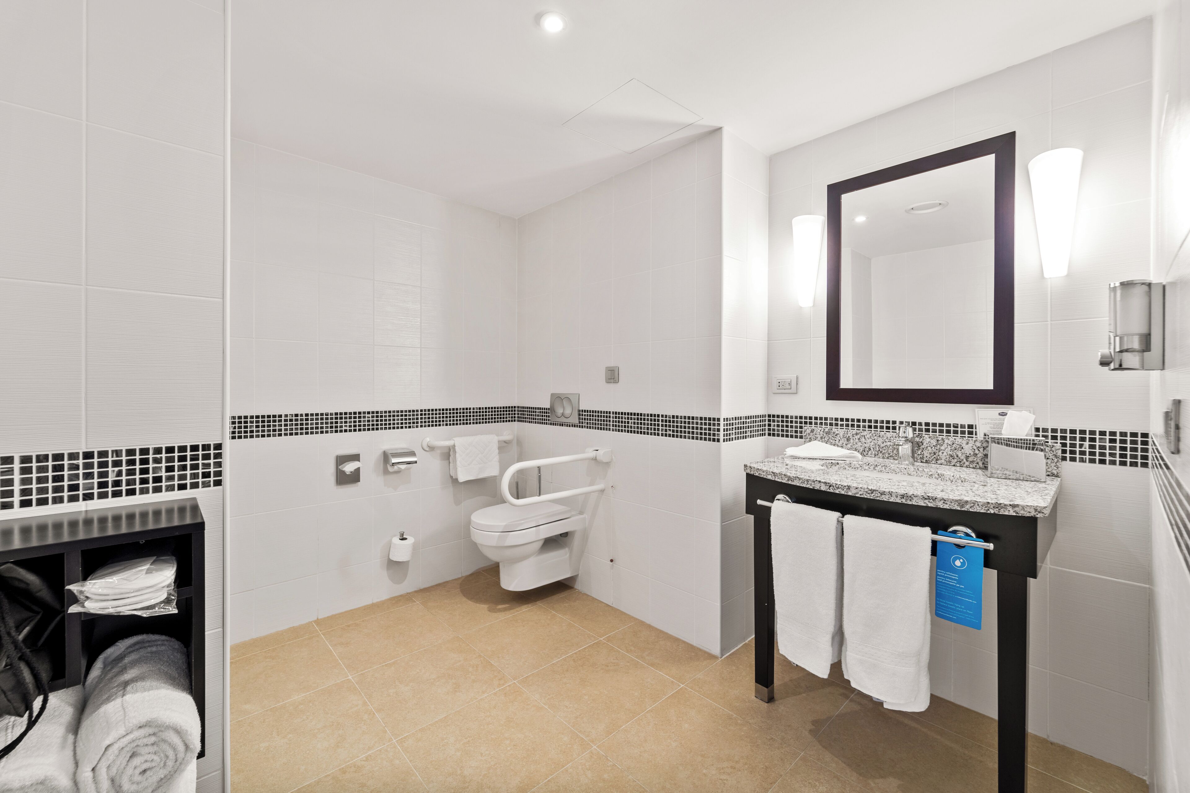 Un bagno moderno con piastrelle bianche, uno specchio con cornice nera, un lavabo con piano in granito e un water con maniglione.