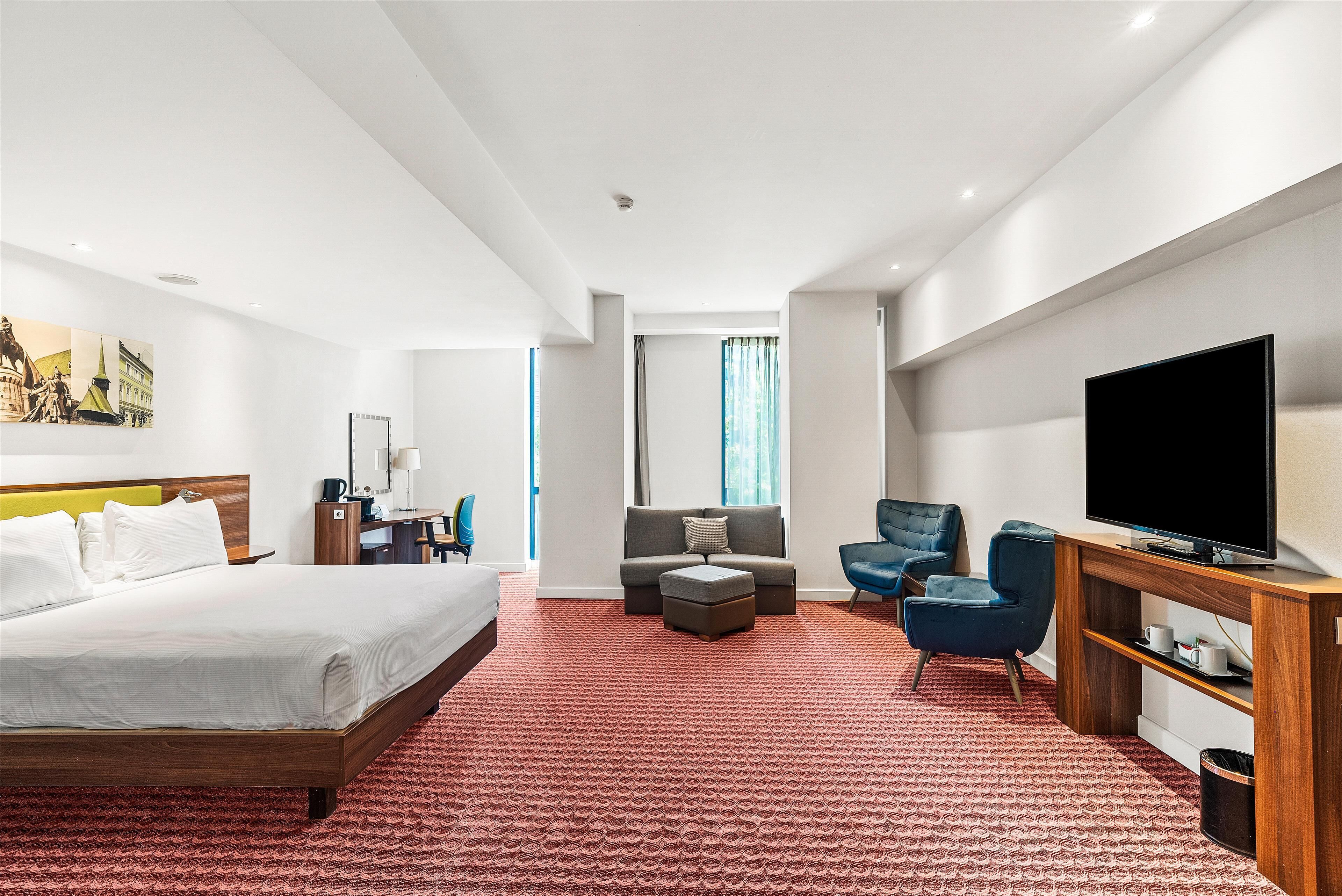 A hotel room with a large bed, a sofa, a TV, and a desk.