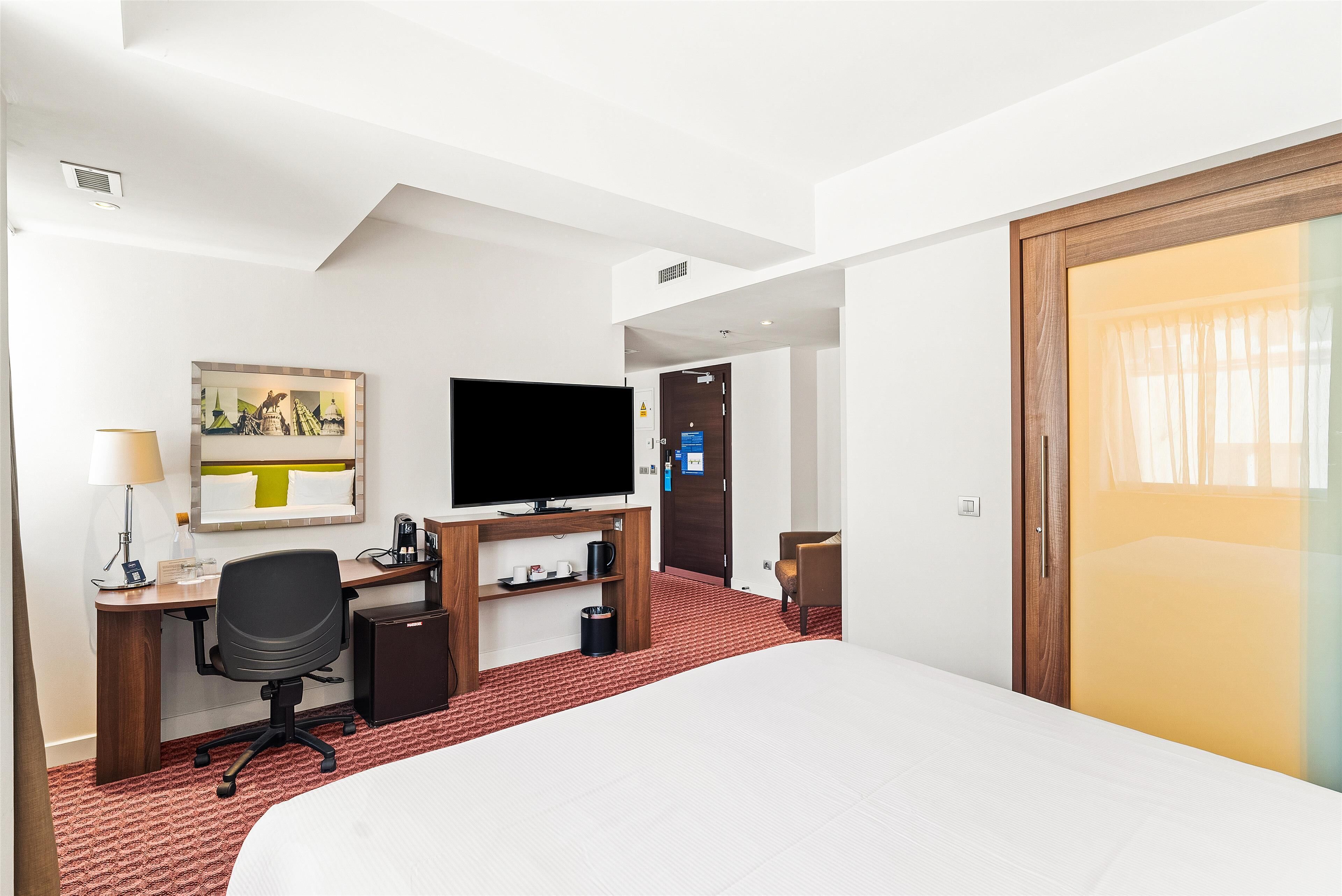 Une chambre d’hôtel comprenant un lit, un bureau avec un ordinateur, une télévision et un petit coin salon.