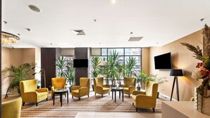 A lobby with yellow armchairs, a reception desk, and large windows with plants. - Hampton by Hilton Cluj-Napoca (Cluj-Napoca)