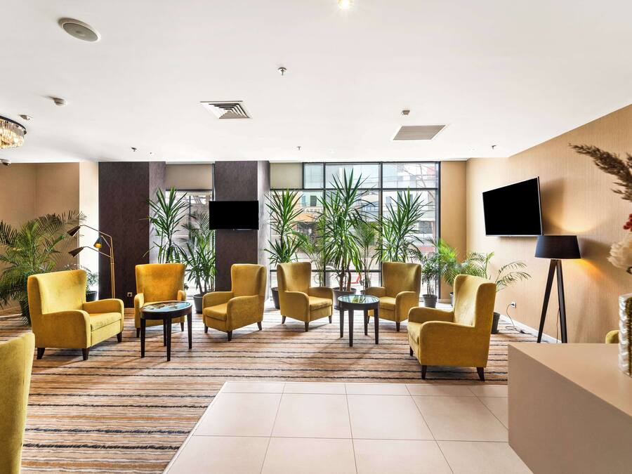 A lobby with yellow armchairs, a reception desk, and large windows with plants.