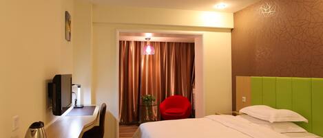 A hotel room with a bed, a desk with a computer, a red chair, a coffee maker, and a telephone.