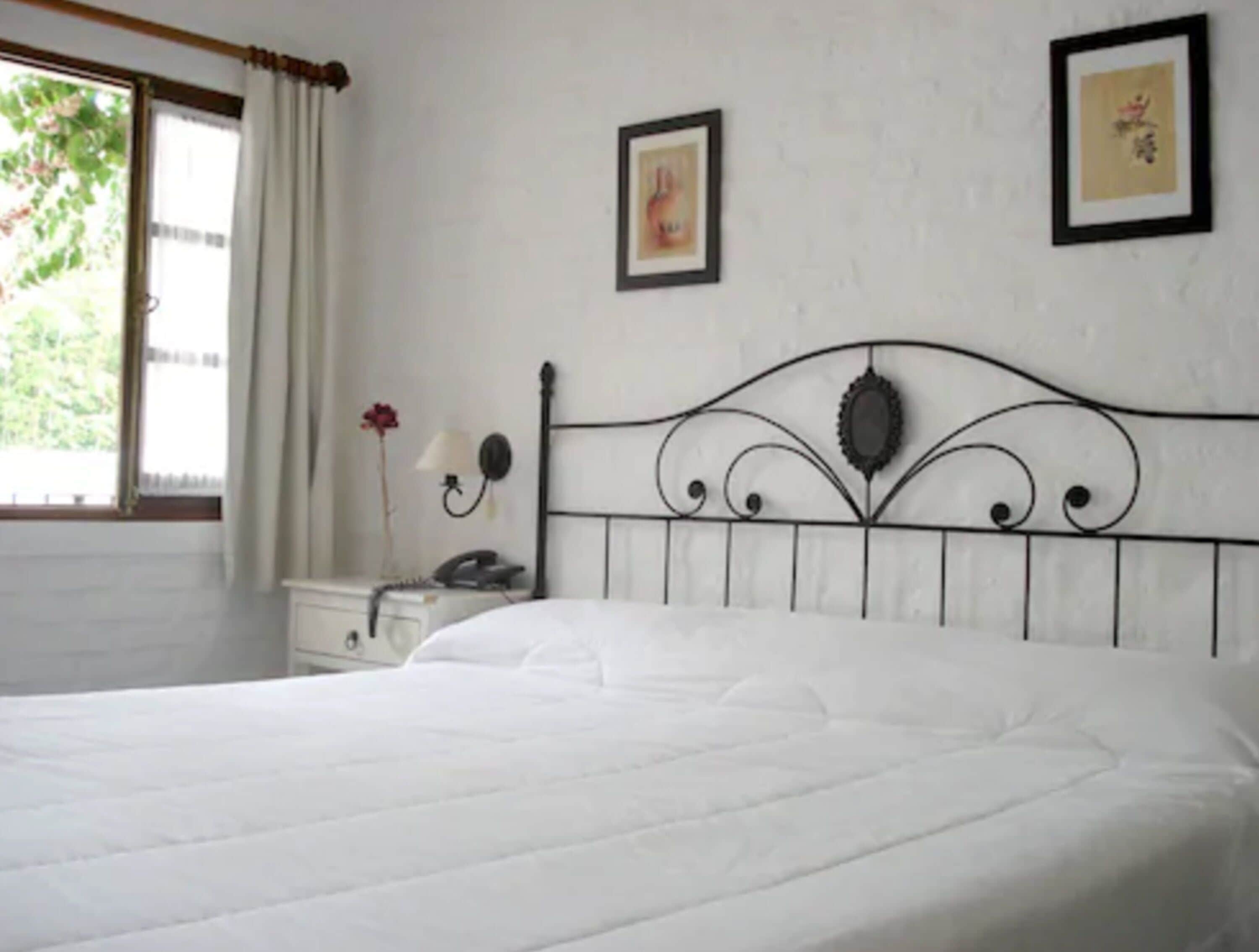 A neatly made bed in a room with a simple headboard, a bedside table with a lamp, and two framed pictures on the wall.