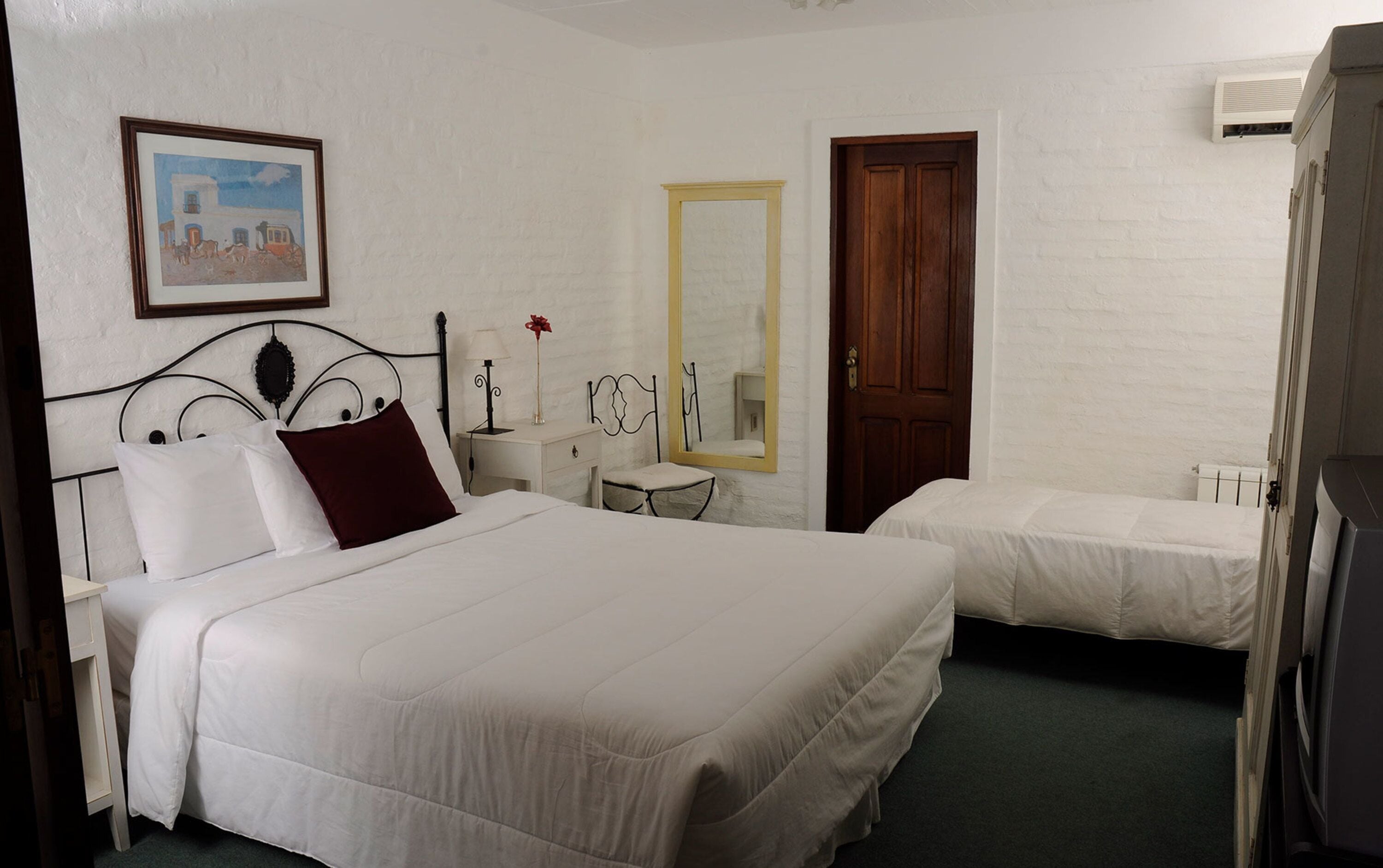 A hotel room with two beds, a wooden door, a white wall, and a framed picture.