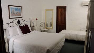 Een hotelkamer met twee bedden, een houten deur, een witte muur en een lijst met een afbeelding.