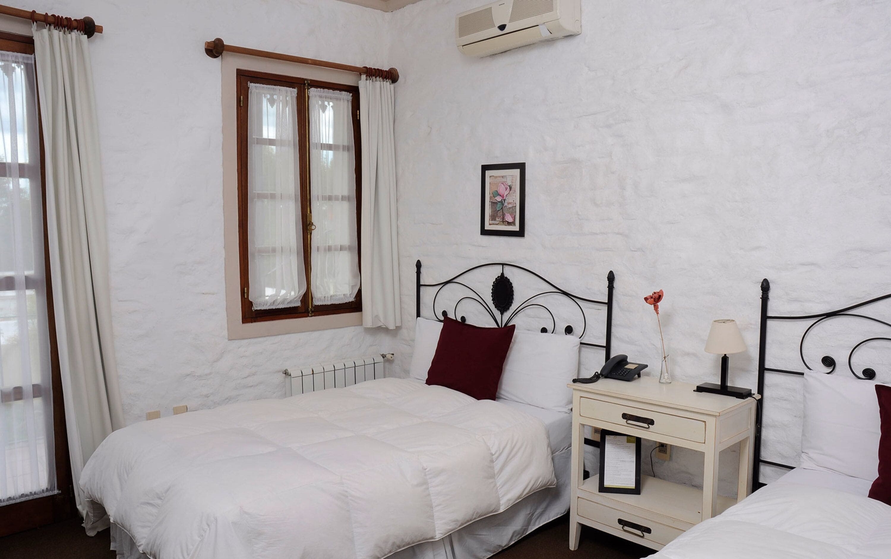 Un dormitorio con una cama individual, una mesita de noche con lámpara, cortinas y una ventana.