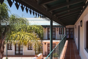 A covered walkway with a tiled floor, a railing, and a view of a building with multiple windows and doors.