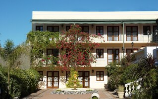 Un edificio de dos pisos con una entrada central, una fuente y un balcón con barandillas.