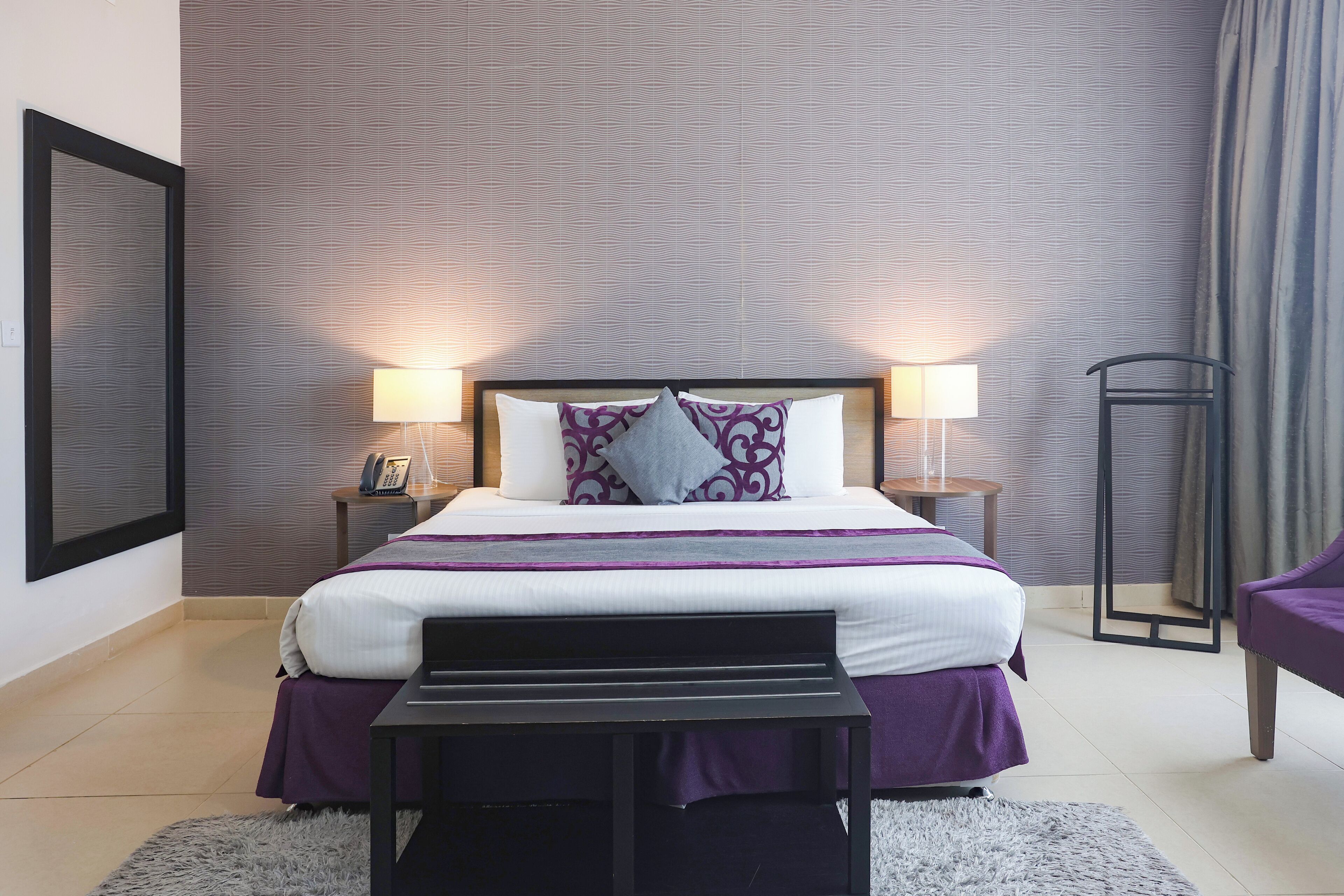 A neatly arranged hotel room with a large bed, two bedside lamps, a nightstand with a phone, and a chair.