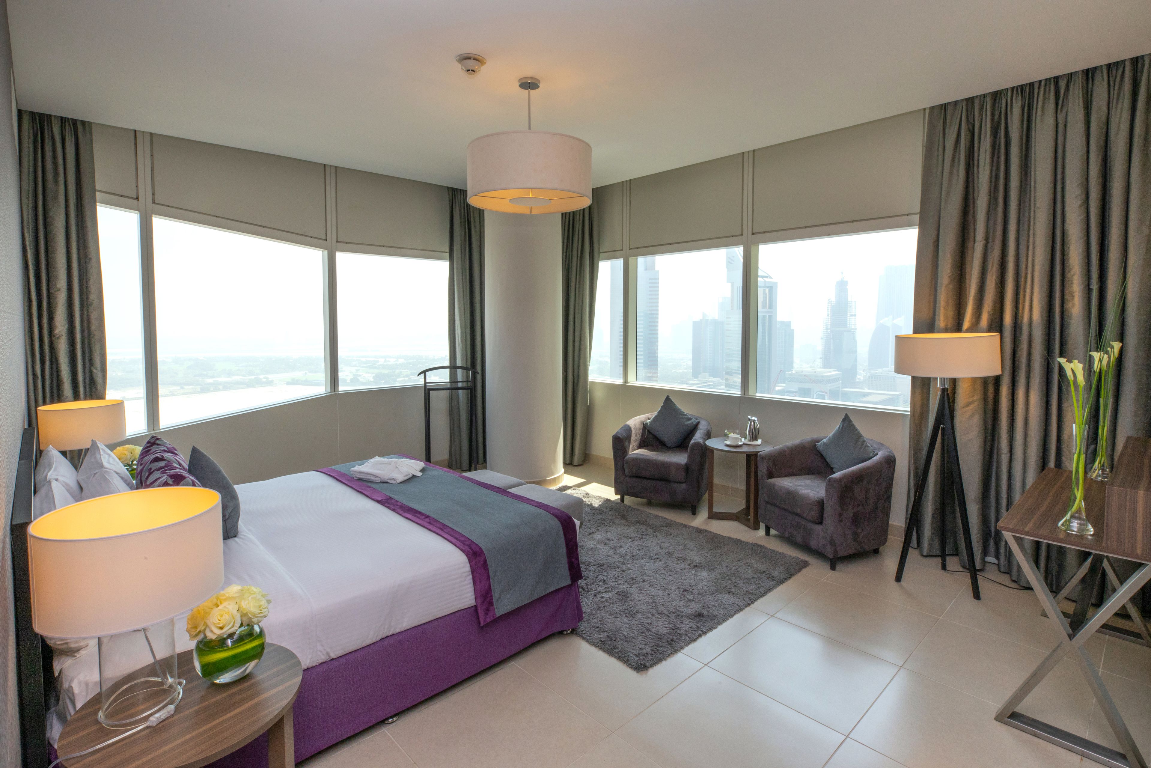 A modern hotel room with a large bed, a sitting area, and a view of the city skyline.